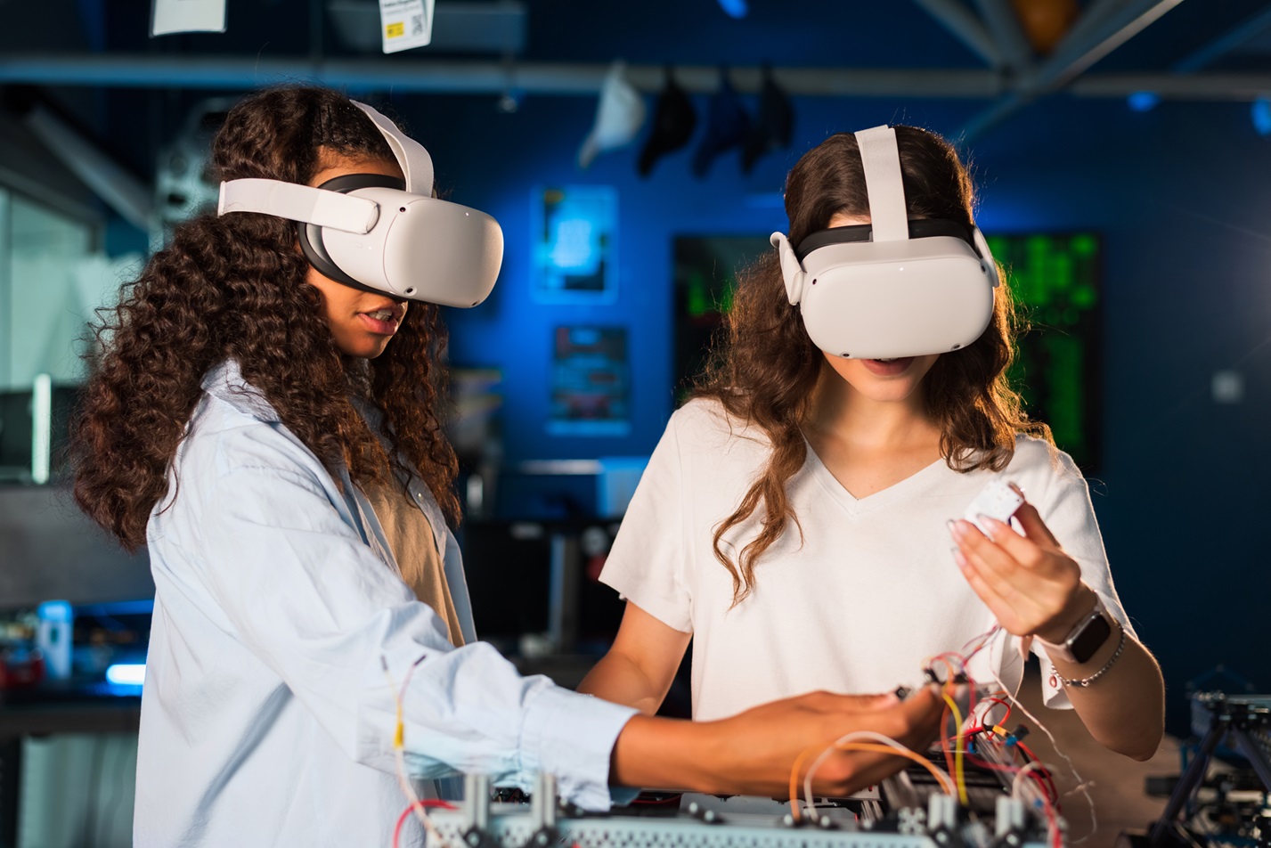 Two young women in VR glasses doing experiments in robotics in a laboratory. Robot on the table
